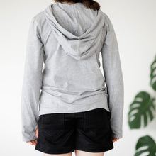 Load image into Gallery viewer, back view of a grey Sensory Friendly Clothing long sleeved hooded t-shirt and black shorts.  The person wearing them also has their thumbs through the thumbholes .  Their posture is relaxed.