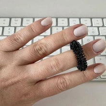 Load image into Gallery viewer, A back Kaiko Spikey Fidget on a person's middle finger.  Their hand is in front of a computer keyboard